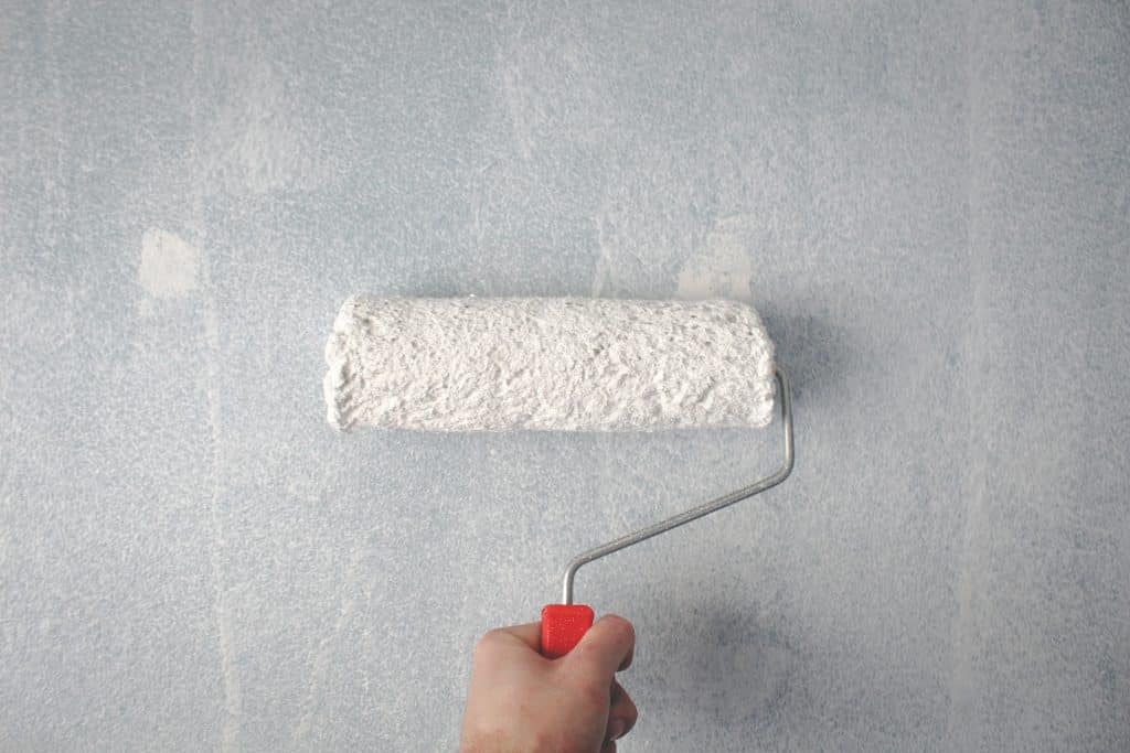 paint roller, handheld, rolling white paint on grey wall